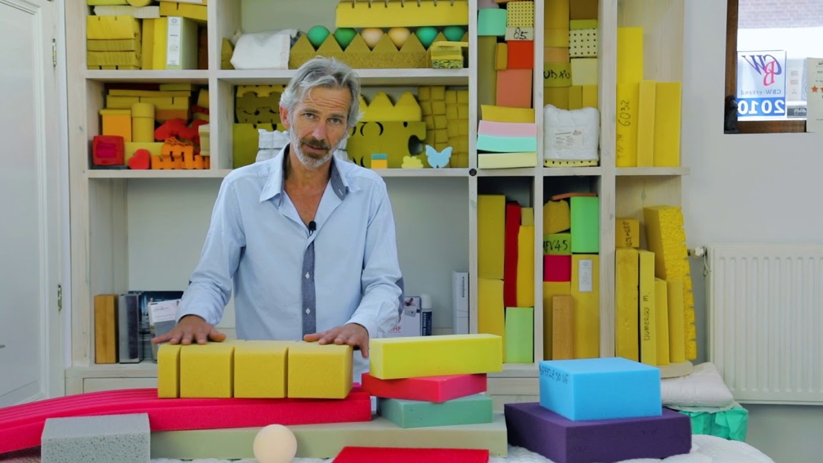 Chris Nederhorst achter een tafel met blokken koudschuim, voor een kast vol schuimmonsters